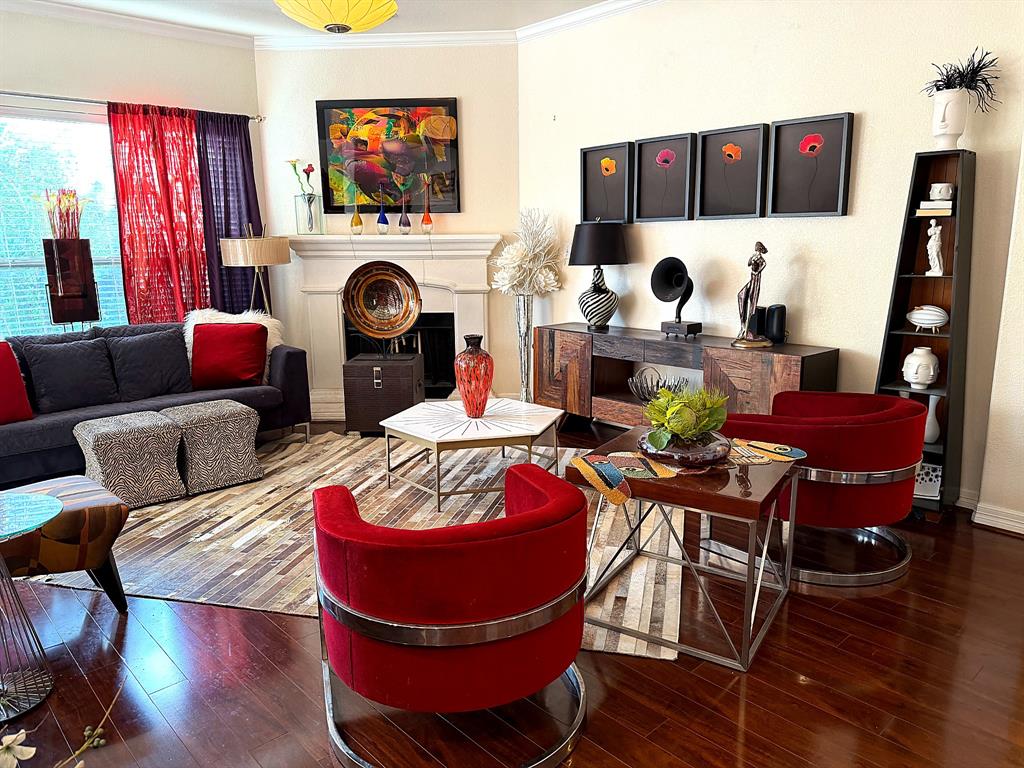Living area featuring wood-finish flooring, a neutral-toned fireplace surround, crown molding, and large window with exterior exposure