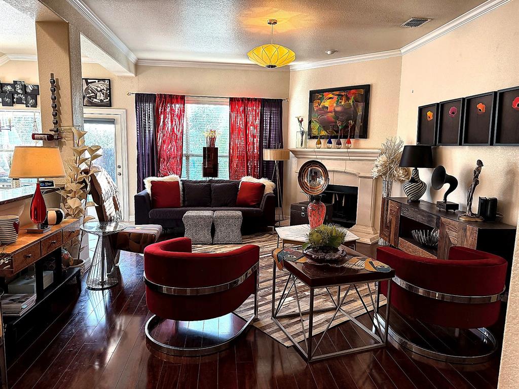 Living space featuring wood-finish flooring, crown molding, and a stone-surround fireplace with an integrated mantel