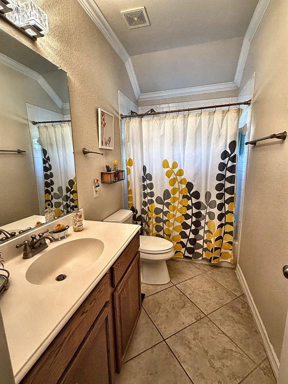 Bathroom featuring a wood-finish vanity with a molded countertop, oval integrated sink, metallic dual-handle faucet, vaulted ceiling, and diagonal-set tile flooring