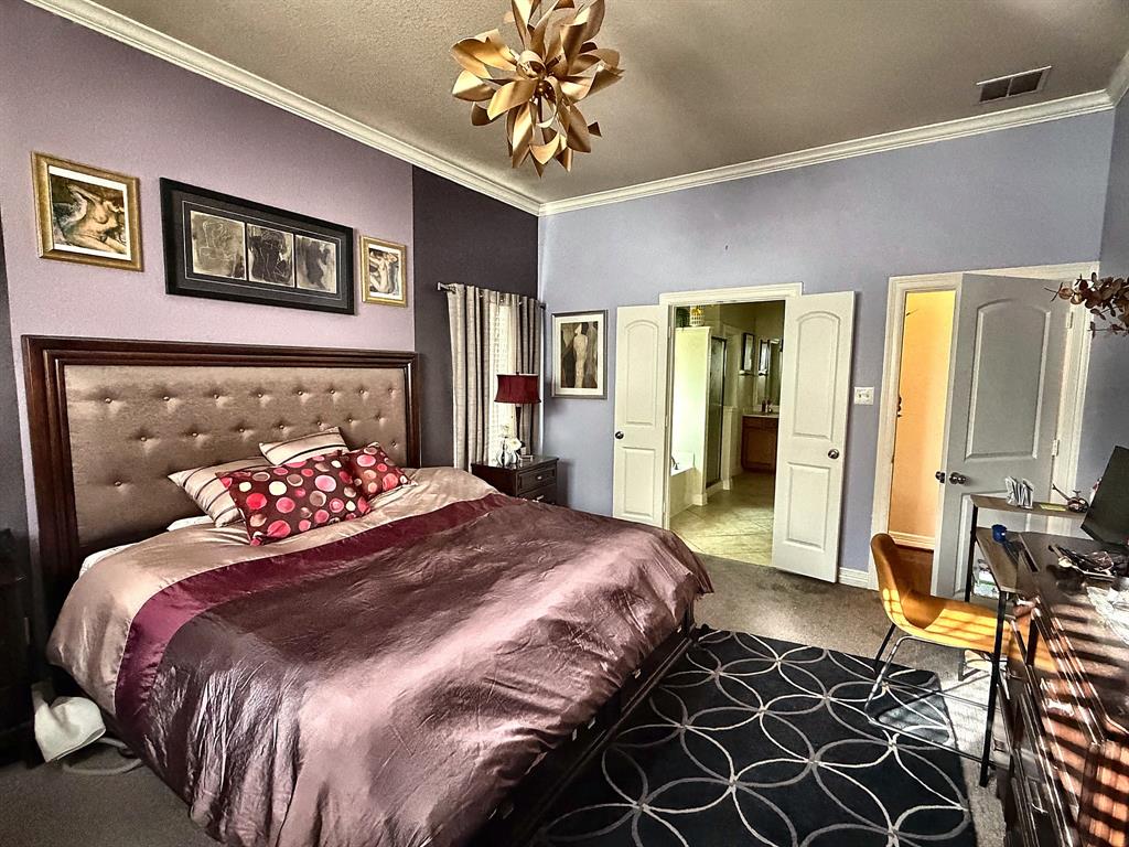 Bedroom featuring crown molding, neutral wall-to-wall carpeting, and a multi-tiered gold-tone geometric ceiling light fixture