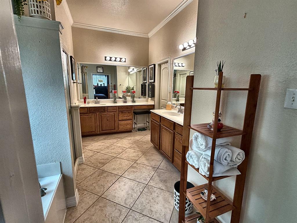 Dual-vanity bathroom featuring wood-finish cabinetry, tile flooring, crown molding, and expansive wall-mounted mirrors