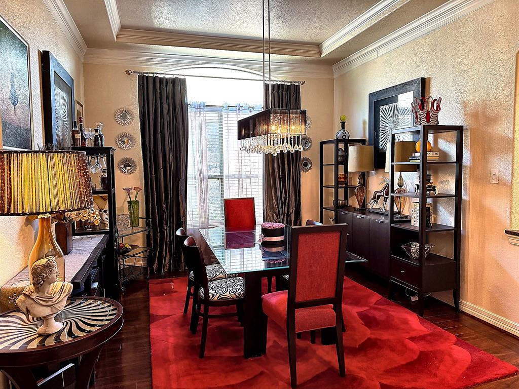 Dining room featuring dark wood-finish flooring, recessed tray ceiling with crown molding, and a rectangular, multi-tiered crystal pendant light fixture