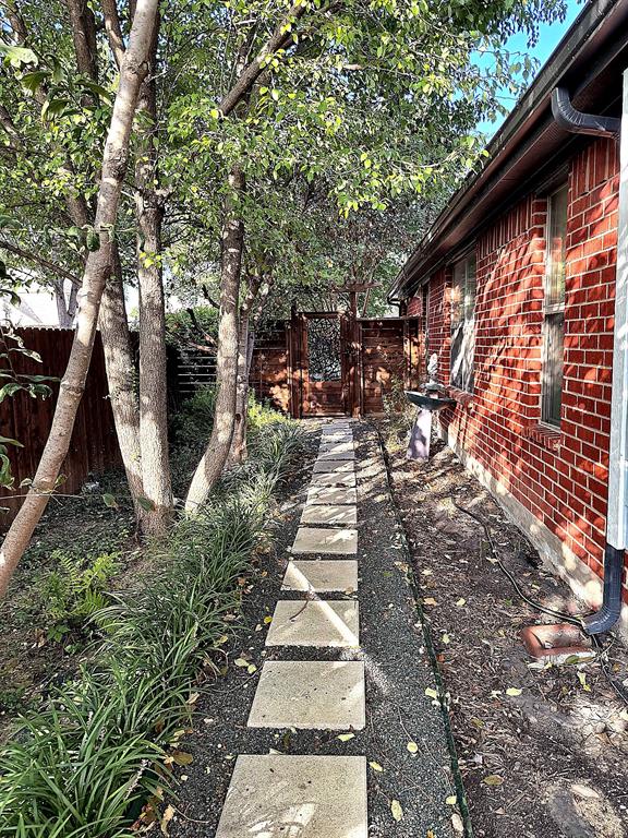Exterior pathway featuring a red brick facade, square stone pavers, gravel landscaping, and a decorative wooden gate