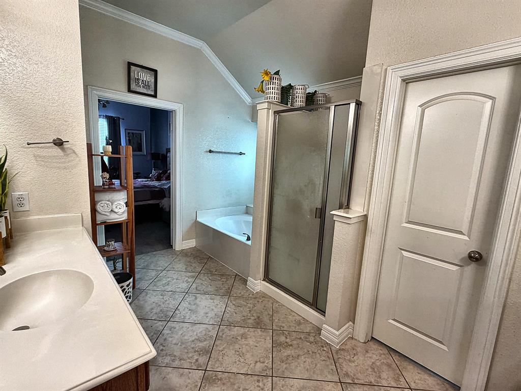 Bathroom featuring a vanity with integrated sink, tiled flooring, soaking tub, and enclosed shower with metallic framing
