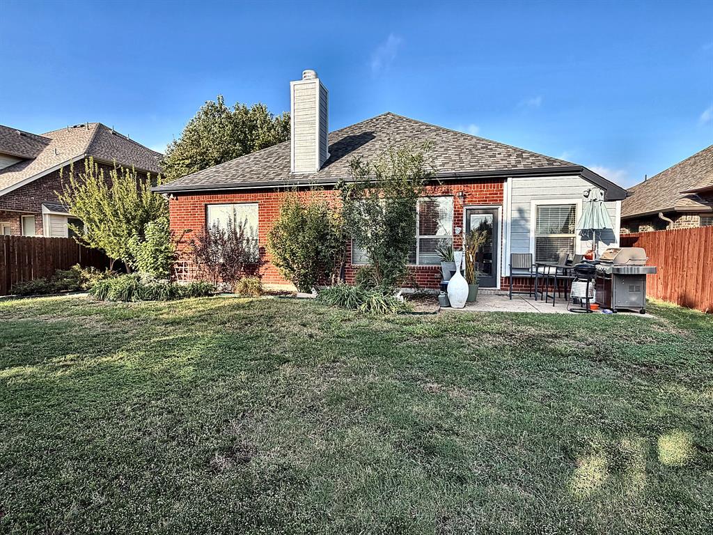 Rear exterior featuring a brick and siding facade, a paved patio, a centered chimney stack, and a fenced backyard