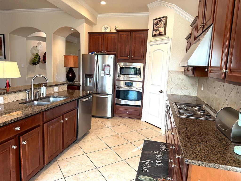 Kitchen featuring dark wood cabinetry, stone countertops, stainless steel appliances, a built-in wall oven and microwave, and tile flooring