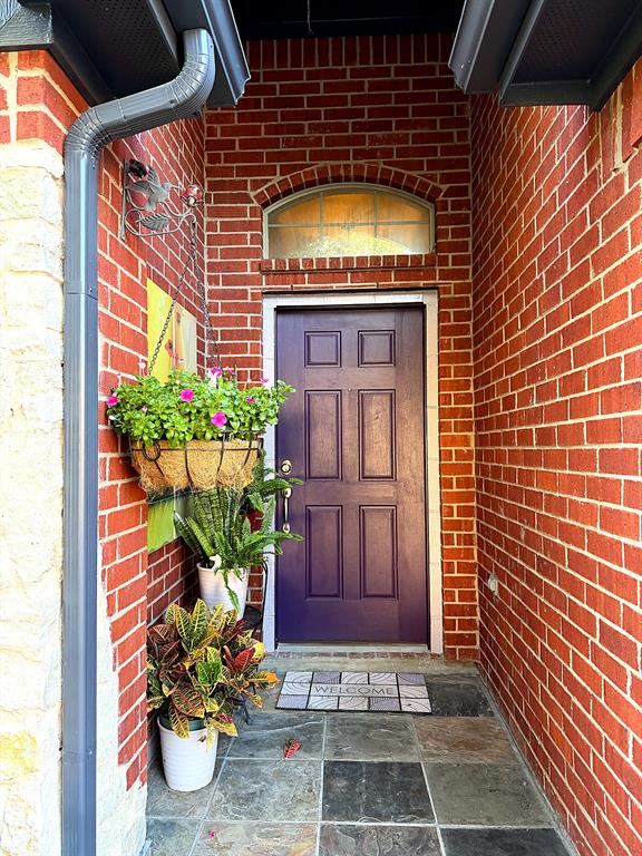 Red brick exterior entryway featuring a six-panel door, arched transom window, and multi-tone stone tile flooring