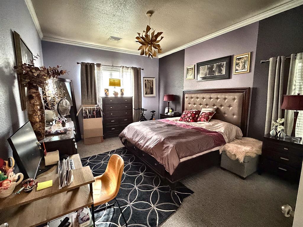 Bedroom featuring crown molding, neutral wall-to-wall carpeting, and a geometric-style pendant light fixture
