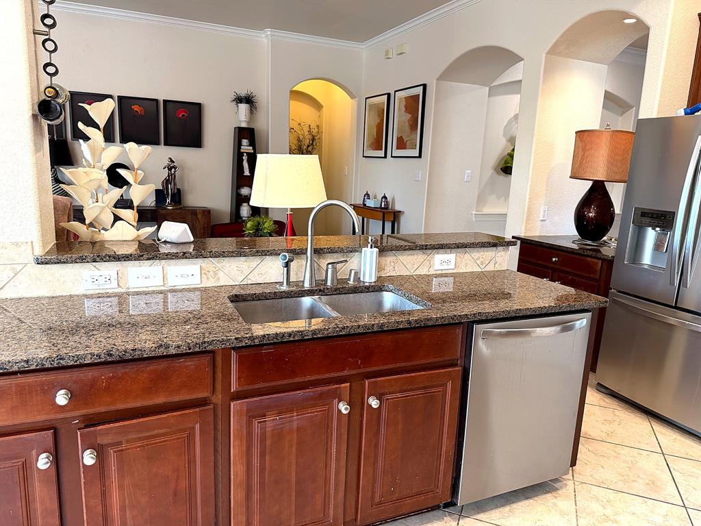 Kitchen featuring dark wood-finish cabinetry, stone countertops, stainless steel appliances, a dual-basin sink, and decorative arched wall niches