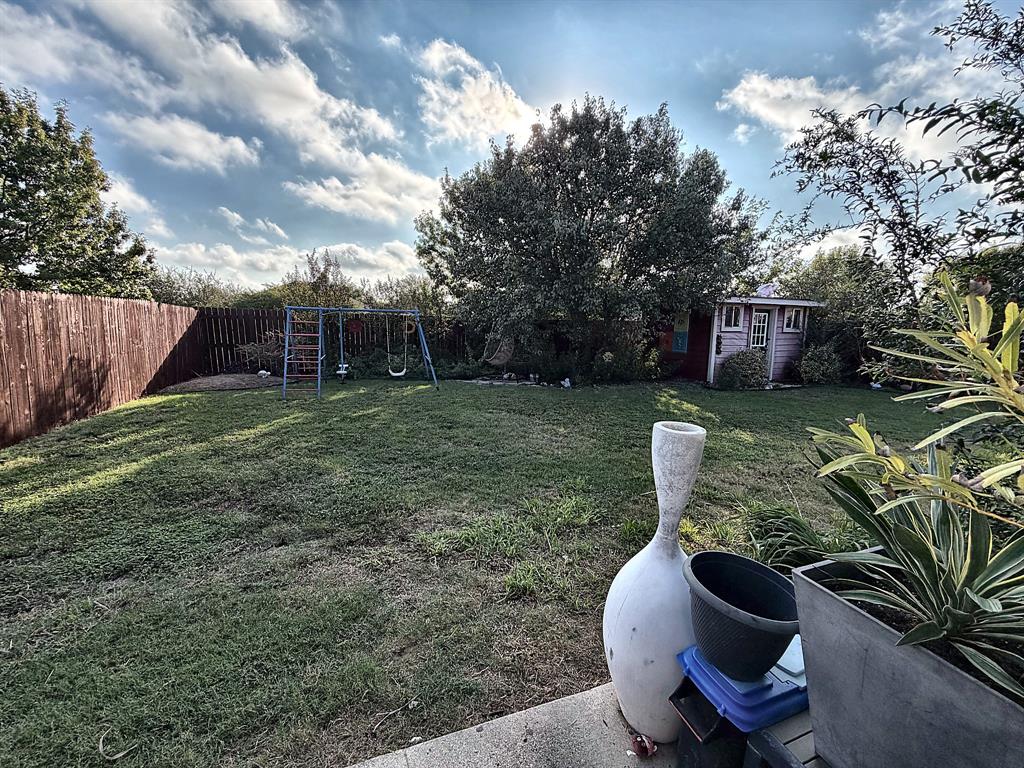 Expansive backyard featuring a level lawn, perimeter wood fencing, mature trees, and a detached outbuilding
