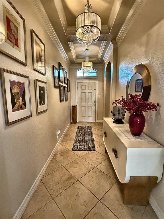 Entryway featuring a coffered ceiling, dual tiered crystal chandeliers, neutral tile flooring laid on a diagonal, and a transom window above the front door