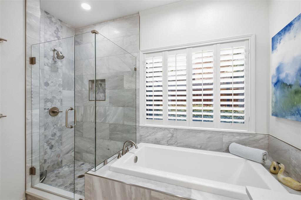 Frameless glass shower with marble-look tile and pebble accents beside a deep soaking tub—your nightly reset.