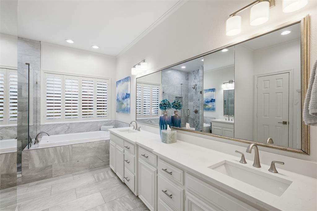 Spa-inspired primary bath with dual sinks, quartz counters, a soaking tub, and frameless glass shower.