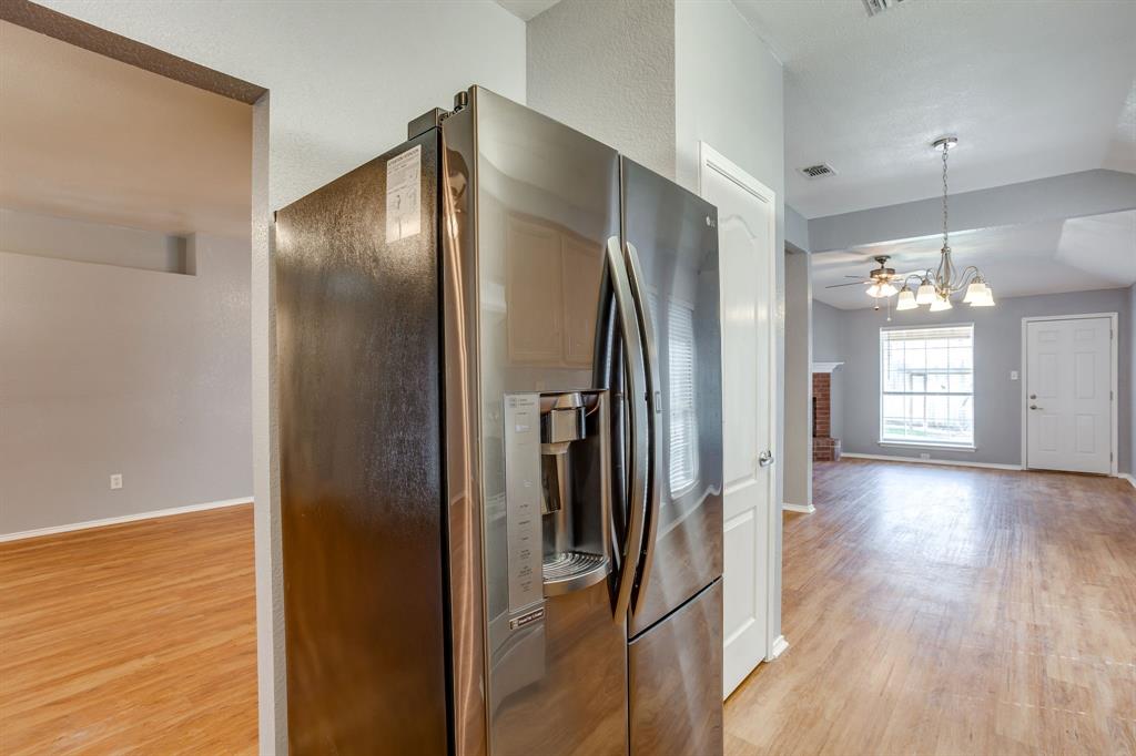 Stainless steel French door refrigerator, wood-finish flooring, multi-light hanging chandelier, and brick-faced fireplace