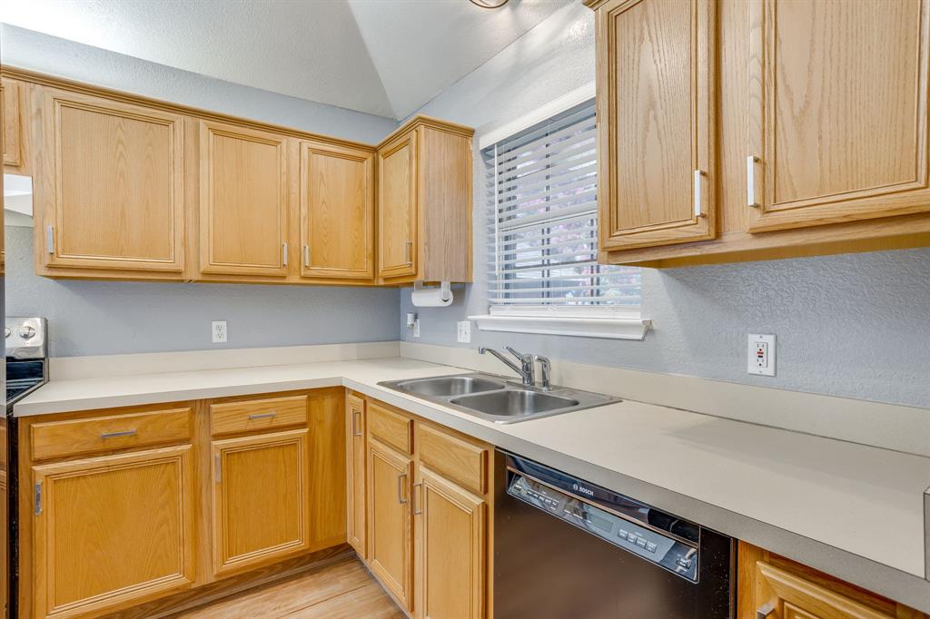 Kitchen featuring wood cabinetry, solid-surface countertops, dual-basin stainless steel sink, and integrated dishwasher