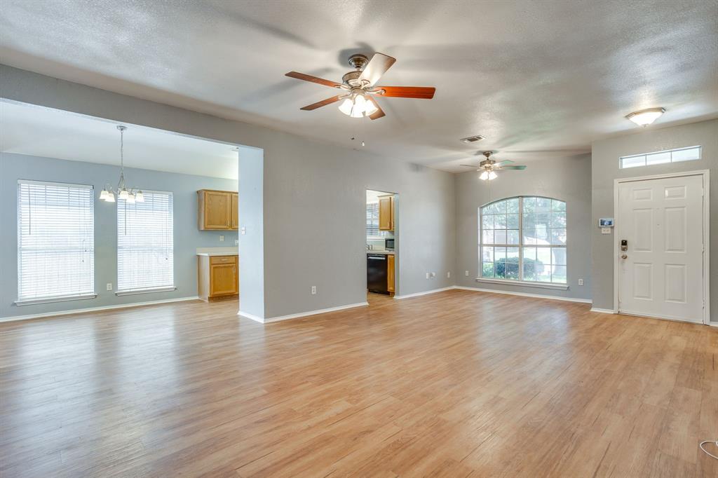 Open-concept interior featuring wood-finish flooring, dual ceiling fans, arched window, and overhead pendant lighting