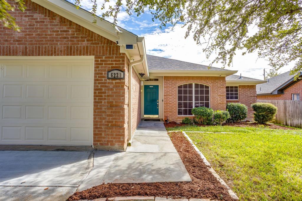 Brick exterior featuring an attached two-car garage, arched window, concrete walkway, and manicured landscaping