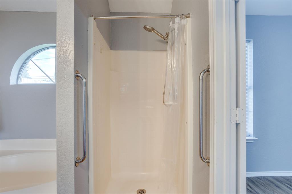 Shower enclosure featuring metal grab bars, adjustable wall-mounted shower head, and arched window