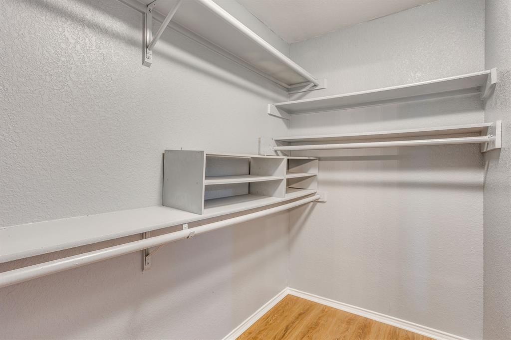 Walk-in storage space featuring wood-finish flooring, white shelving tiers, and multiple built-in garment rods