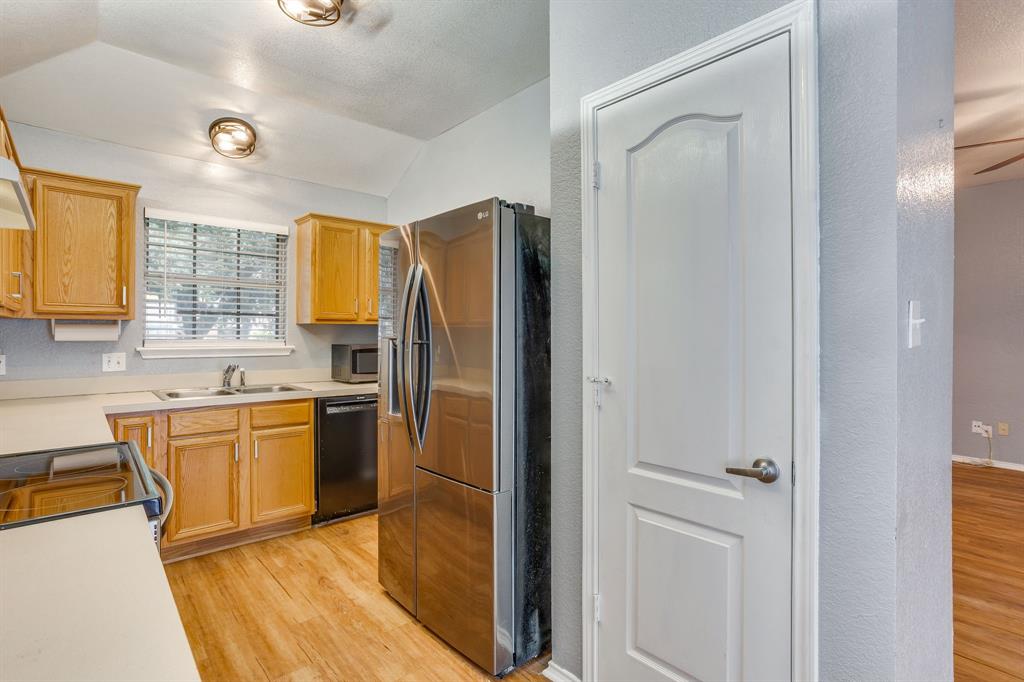 Kitchen featuring shaker-style cabinetry, stainless steel refrigerator, solid-surface countertops, dual-basin stainless steel sink, and wood-finish flooring