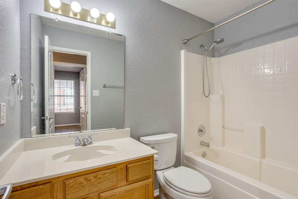 Bathroom featuring a wood-finish vanity with a seamless integrated countertop and sink, wall-mounted four-light fixture, large rectangular vanity mirror, and a tub-shower combination with a showerhead attachment