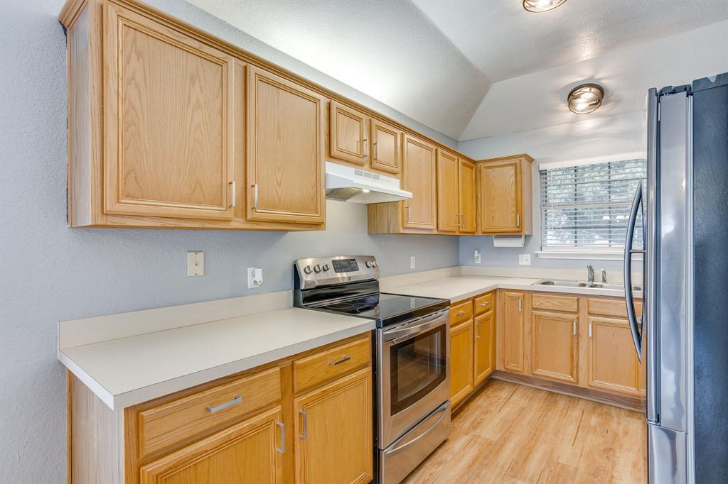 Kitchen featuring wood cabinetry, stainless steel appliances, solid-surface countertops, wood-finish flooring, and a vaulted ceiling