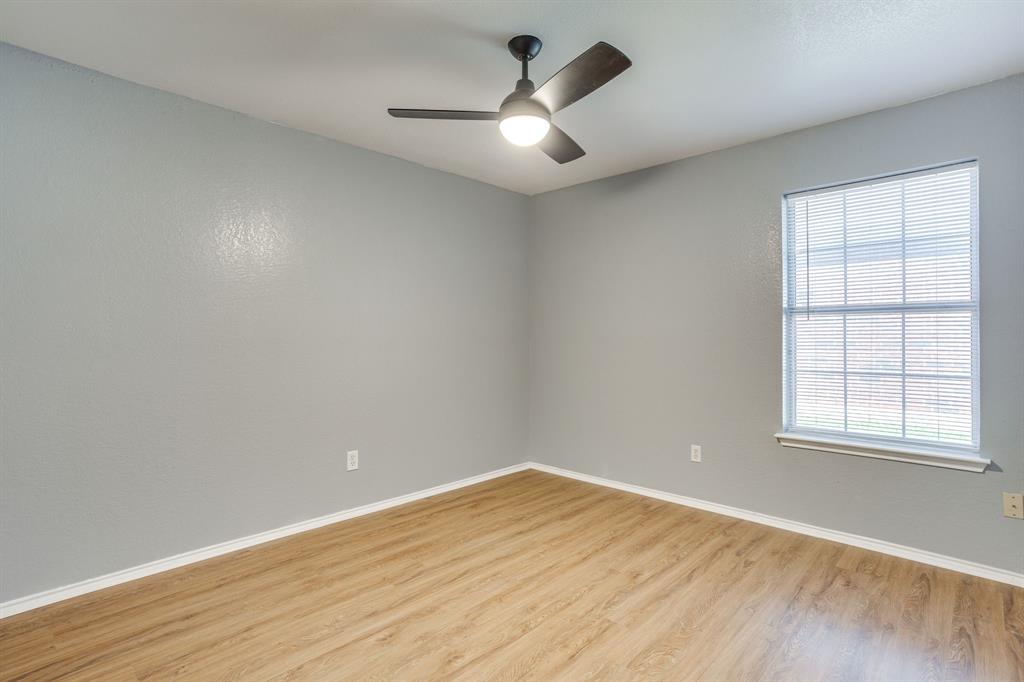 Interior room featuring light-toned walls, wood-finish flooring, a single window with horizontal blinds, and a dark-finish ceiling fan with integrated lighting