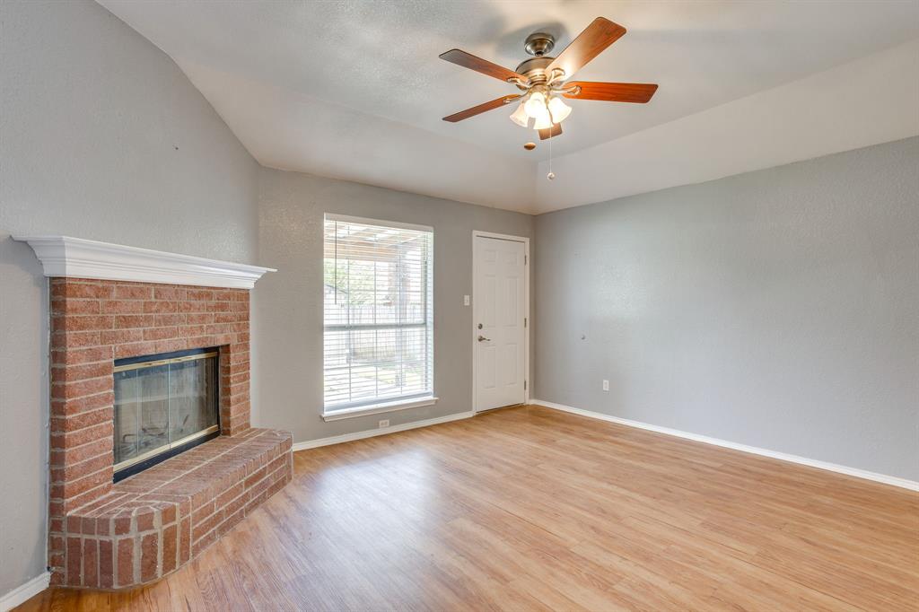 Vaulted ceilings, red brick fireplace with a white mantel, wood-finish flooring, and a ceiling fan with integrated lighting