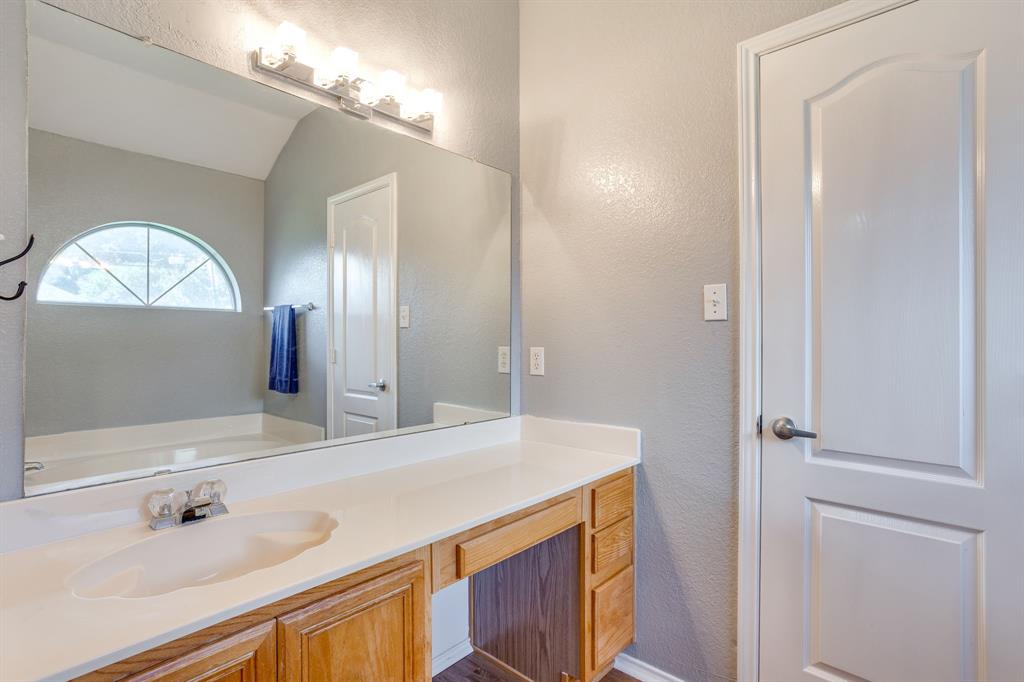 Bathroom vanity with a solid-surface countertop, integrated sink, wood-finish cabinetry, a large wall-mounted mirror, and an arched window