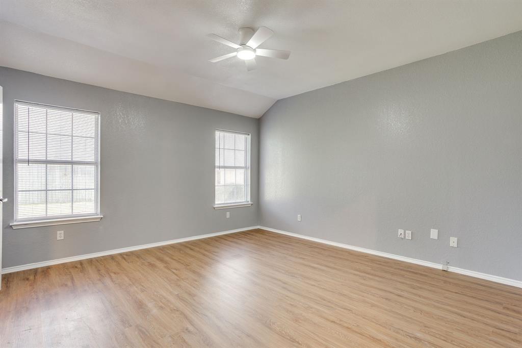 Room featuring wood-finish flooring, vaulted ceilings, neutral wall paint, two grid-pattern windows, and a central ceiling fan with integrated lighting