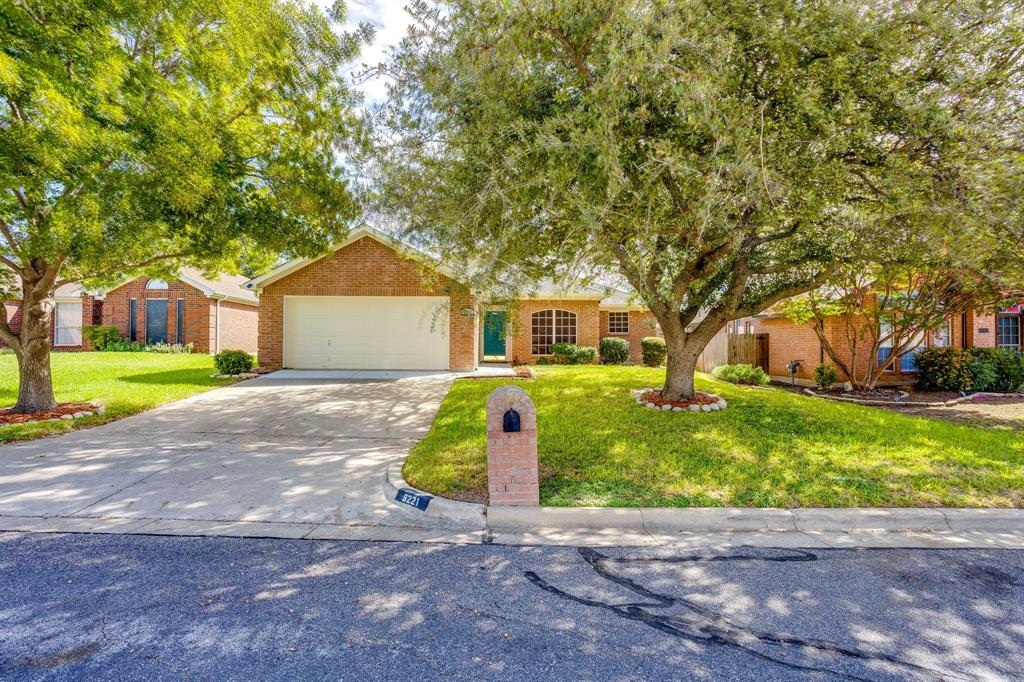 Single-story brick exterior featuring a multi-car garage, arched window accents, mature trees, and a concrete driveway