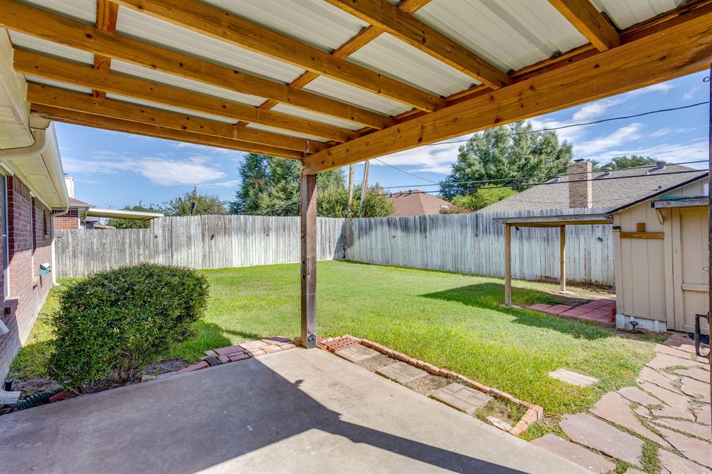 Covered patio featuring an exposed wood-beam ceiling, concrete flooring, stone-bordered landscaping, and a fenced backyard