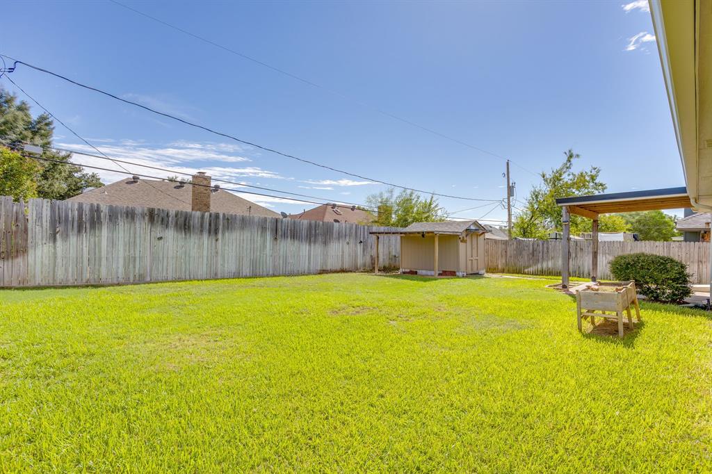 Backyard featuring a grass lawn, perimeter wood fencing, a storage shed, and a covered patio area
