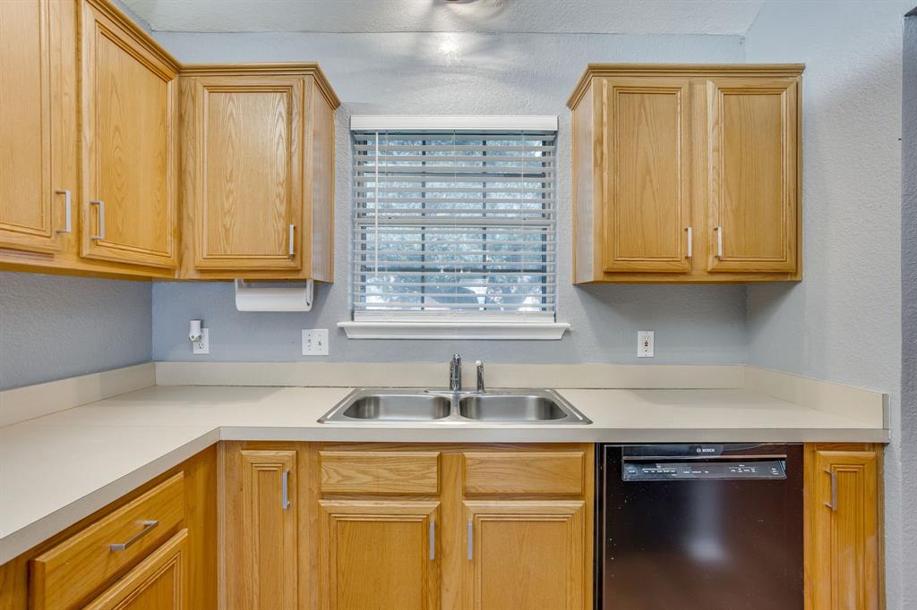 Kitchen featuring natural wood-finish cabinetry, solid-surface countertops, dual-basin stainless steel sink, and built-in black dishwasher