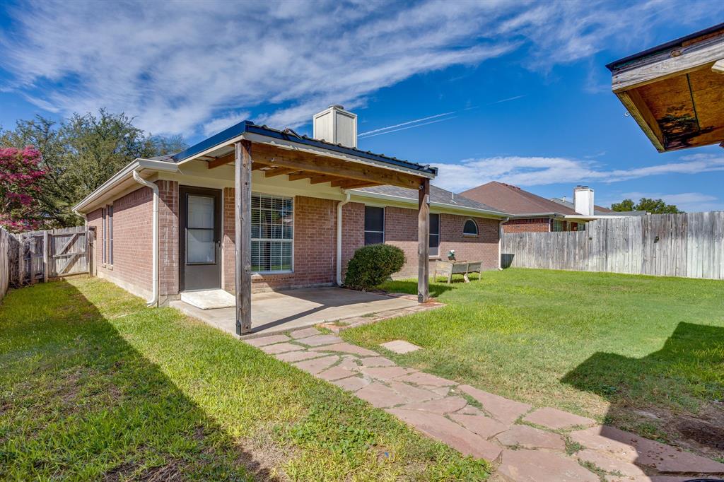 Exterior brick facade featuring a covered concrete patio, stone walkway, and perimeter wood fencing