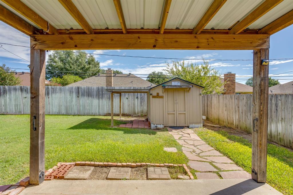 Covered patio with exposed timber framing, detached storage shed, stone paver walkway, and wood privacy fencing
