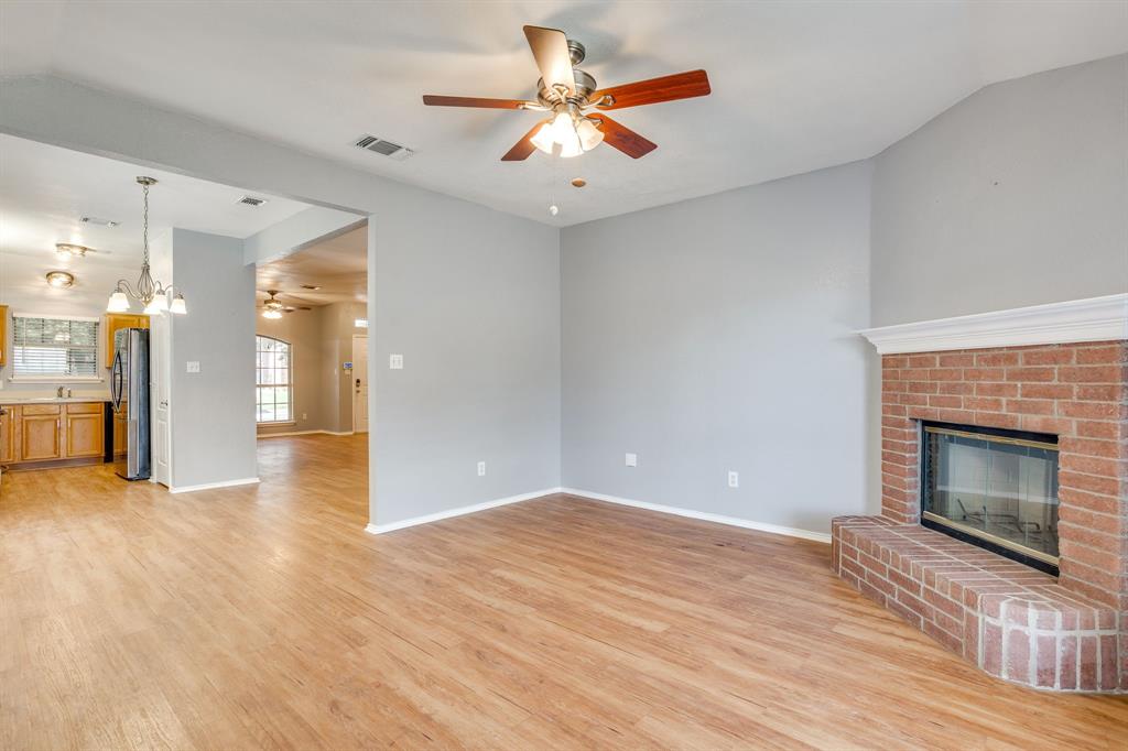 Red brick fireplace with a decorative mantel, wood-finish flooring, and ceiling fan with integrated lighting