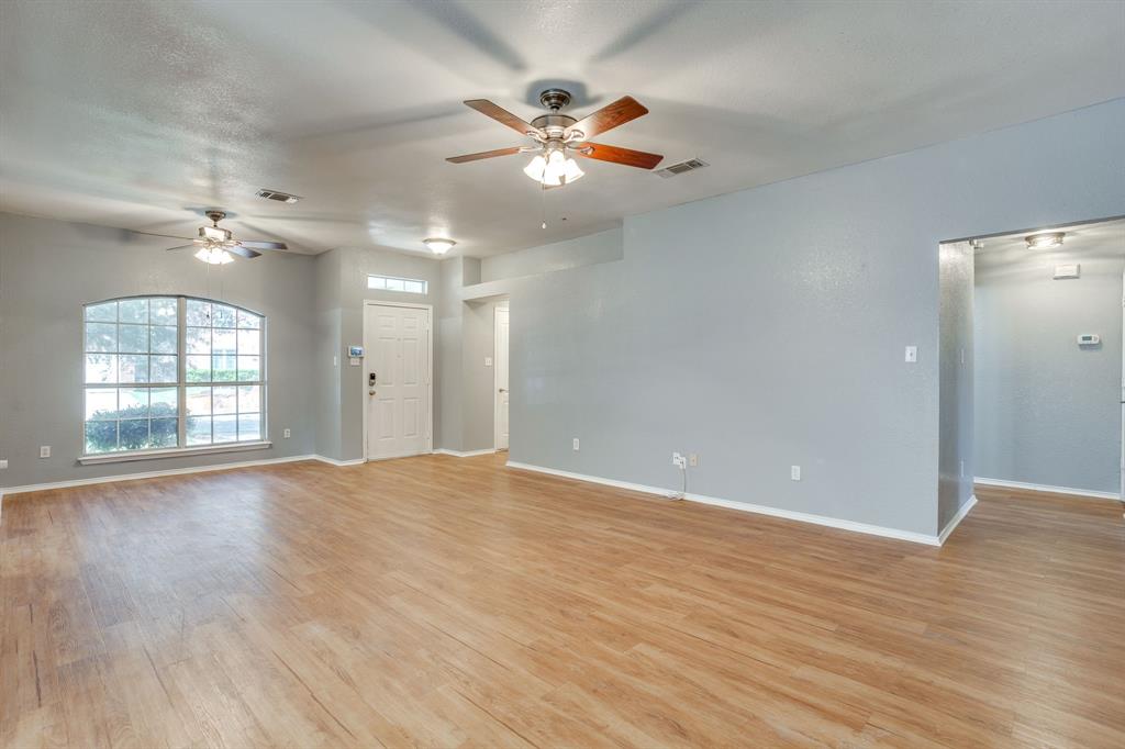 Interior featuring wood-finish flooring, two ceiling fans with integrated lighting, a multi-pane arched window, and a paneled entry door with a transom window