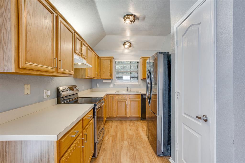 Kitchen featuring light wood-finish cabinetry, neutral solid-surface countertops, stainless steel appliances, wood-finish flooring, and recessed ceiling lighting