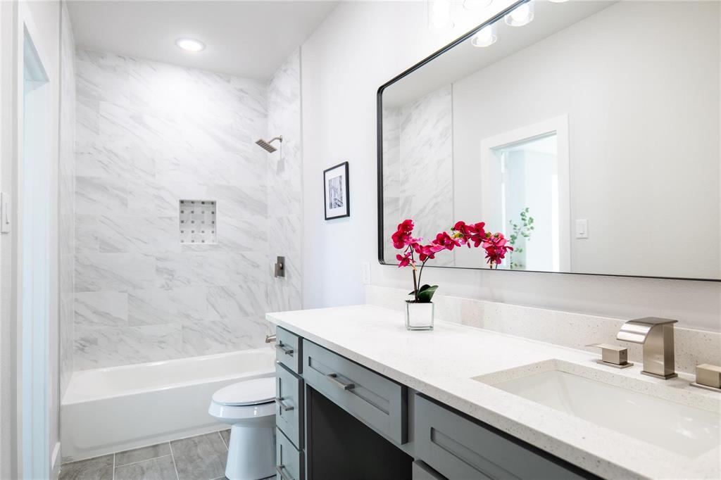 Bathroom featuring a gray vanity with a quartz countertop, rectangular under-mount sink, large-format tile tub surround with an integrated niche, and a wide wall-mounted mirror