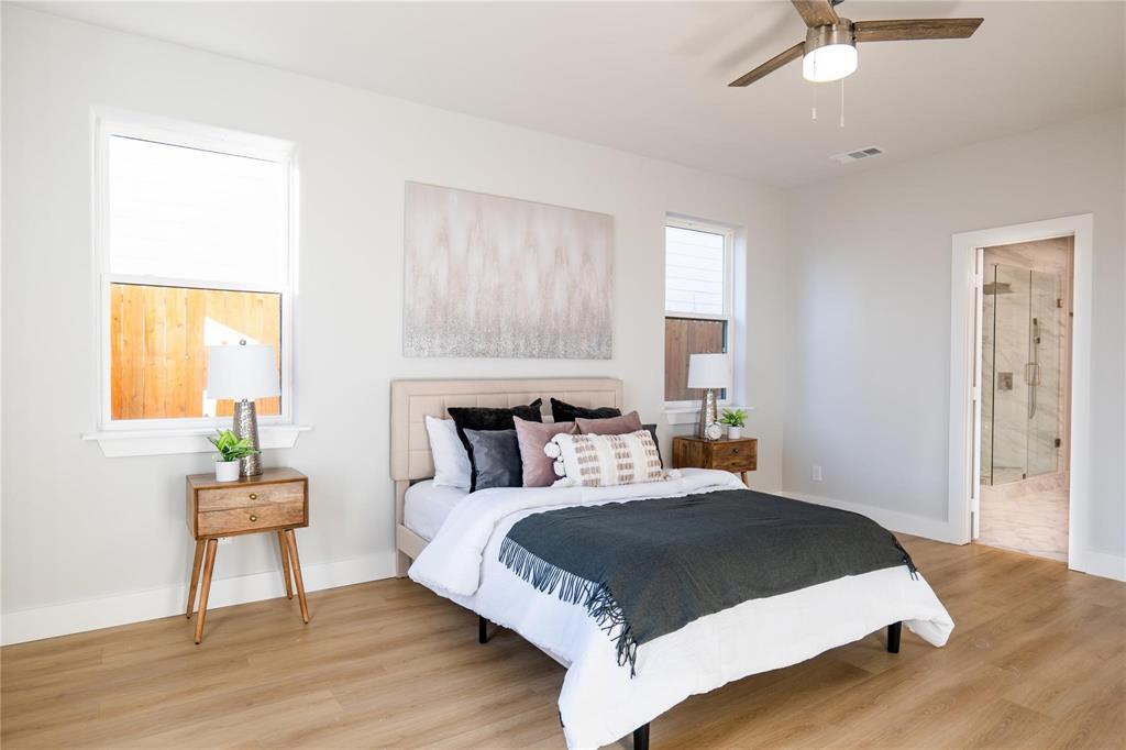 Neutral-toned bedroom featuring wood-finish flooring, dual windows, and an integrated ceiling fan with light fixture