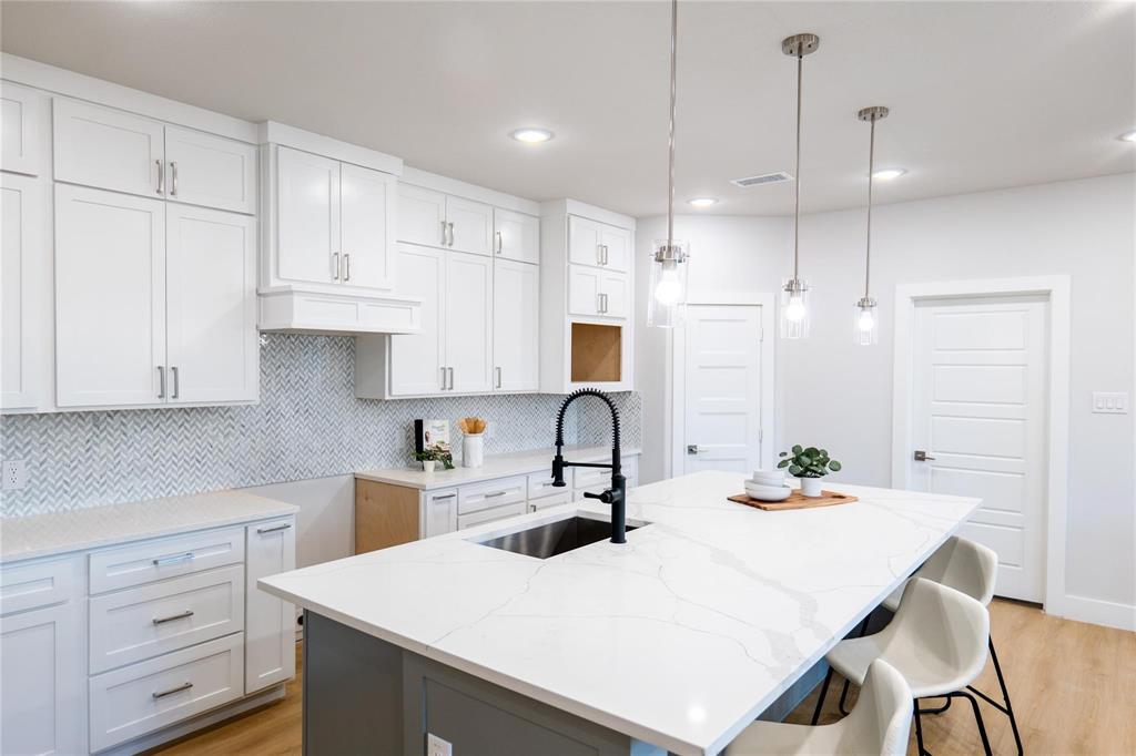 Kitchen featuring white shaker-style cabinetry, quartz countertops with a veined pattern, herringbone-patterned backsplash tile, center island with an undermount sink and matte black faucet, and three pendant lights