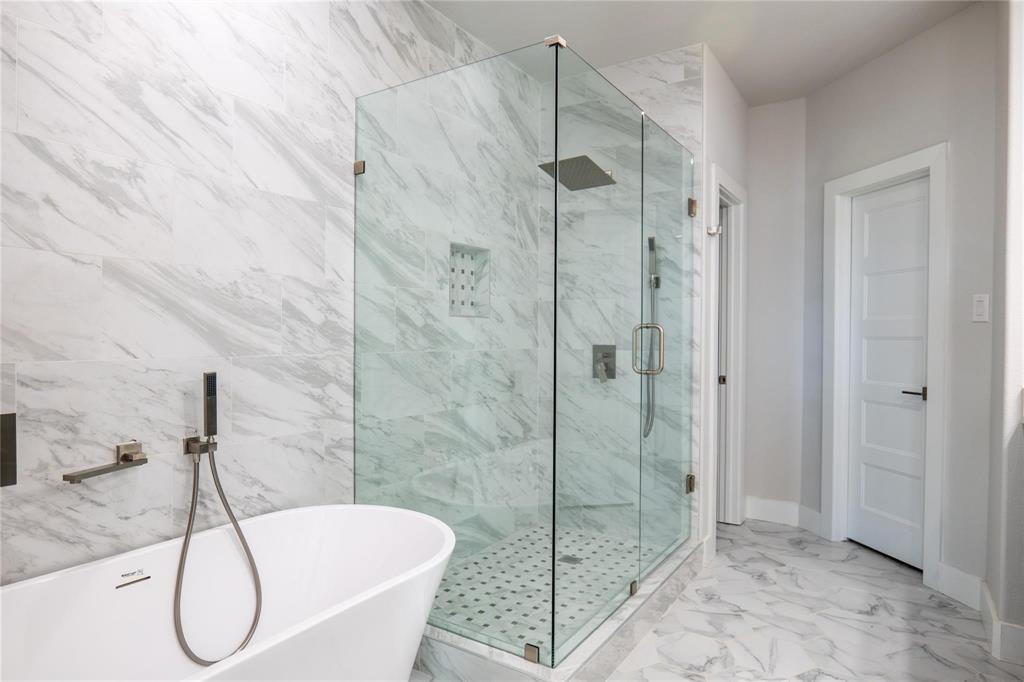 Freestanding soaking tub with wall-mounted hand shower, glass-enclosed shower with tiled walls, rainfall showerhead, and patterned tile flooring