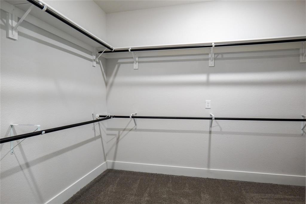 Walk-in closet featuring two-tier storage, wall-mounted white shelving, dark finish metal hanging rods, and carpeted flooring