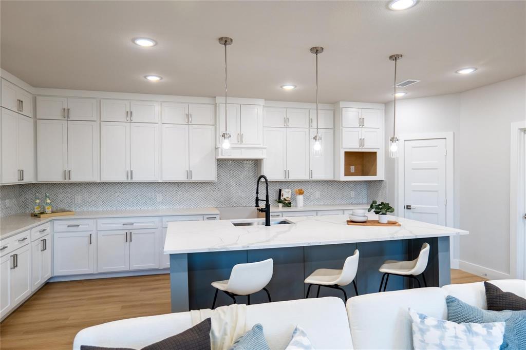 Kitchen featuring white cabinetry, center island with stone-finish countertop, herringbone-patterned tile backsplash, pendant lighting, and wood-finish flooring