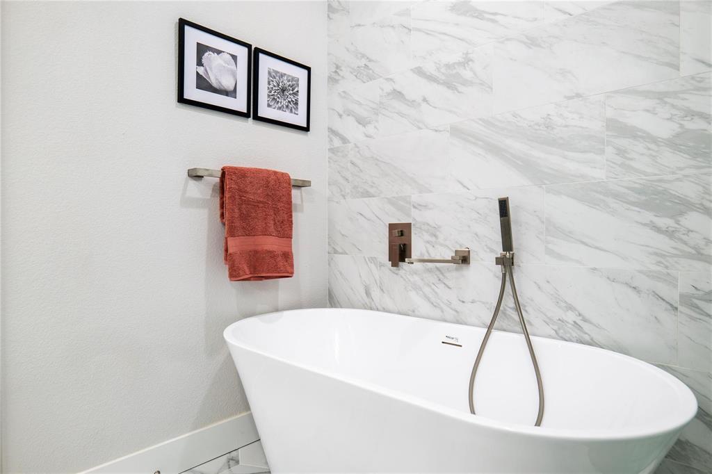 Freestanding soaking tub featuring a wall-mounted matte metal faucet, handheld shower wand, and floor-to-ceiling large-format stone-finish tile surround