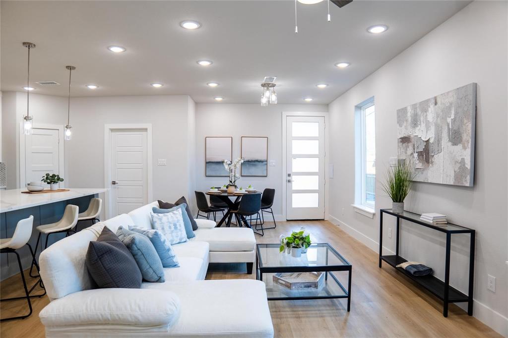 Open-concept interior featuring wood-finish flooring, recessed lighting, a central island with waterfall-edge countertop, and a multi-pane glass entry door