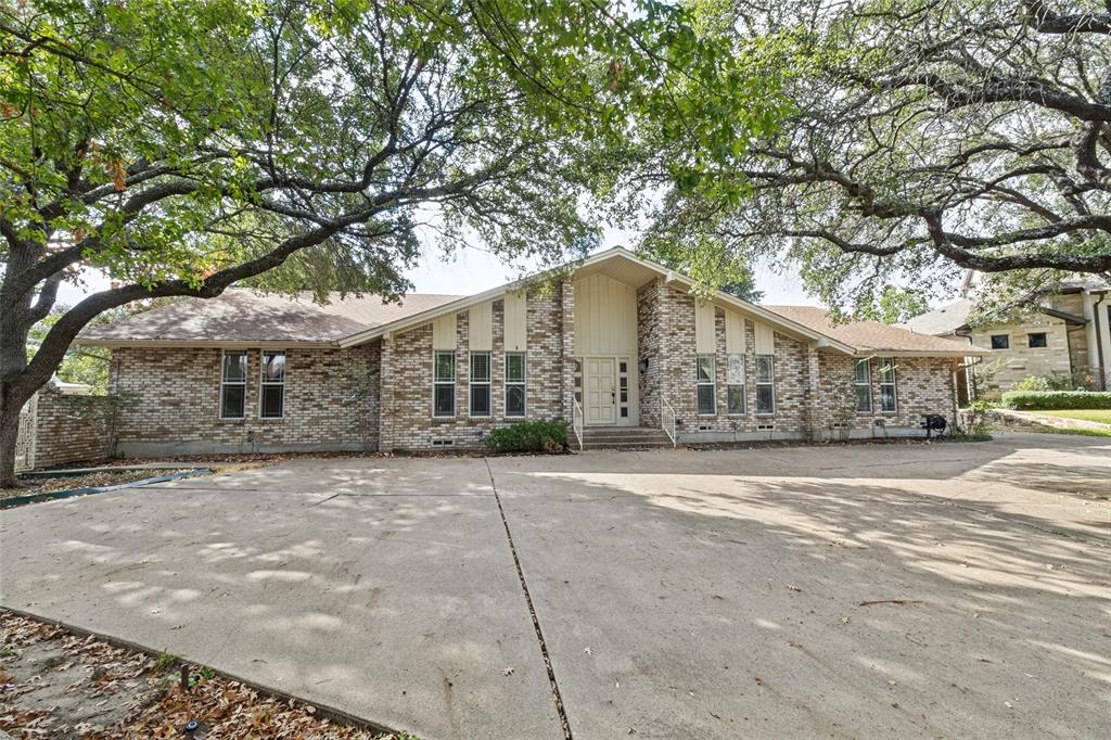 Single-story brick exterior featuring a multi-gabled roofline, circle driveway, and mature canopy trees