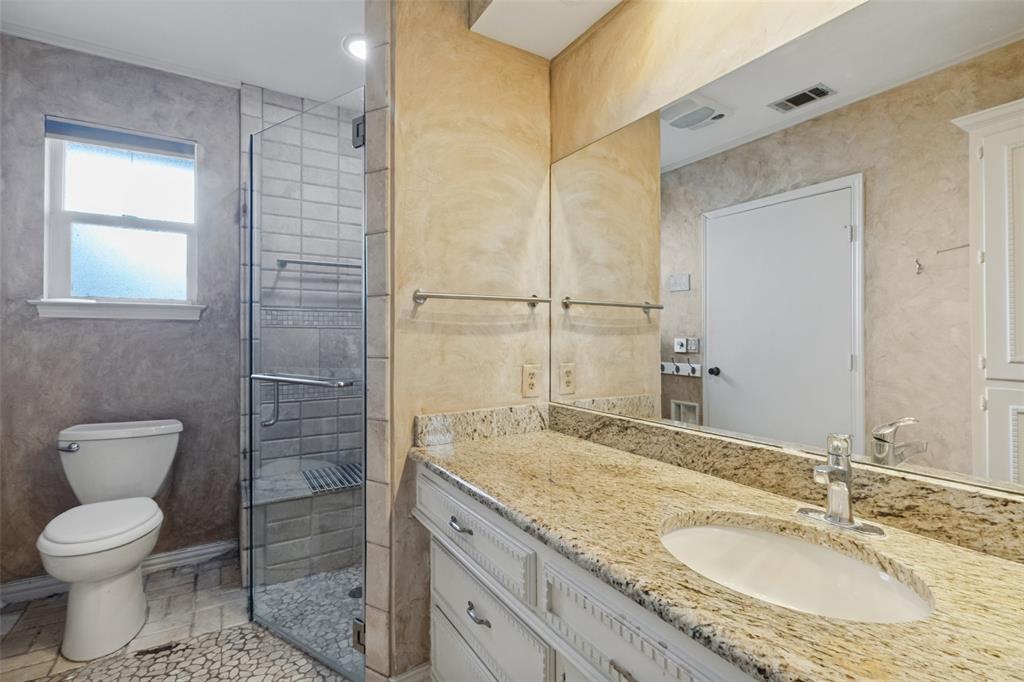 Vanity featuring granite countertop, undermount sink, and white cabinetry, complemented by a walk-in shower with glass enclosure and pebble-stone flooring