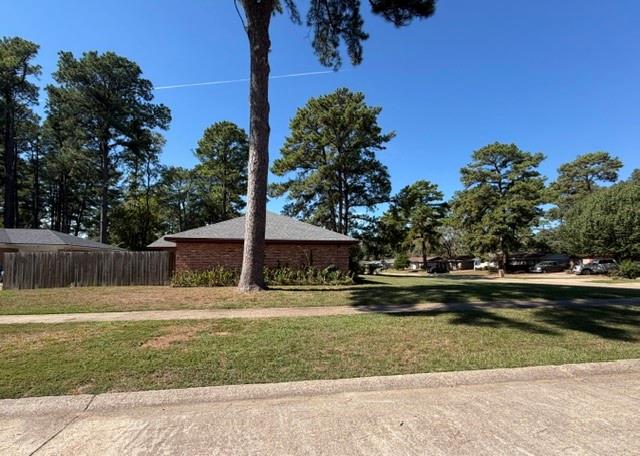 Brick exterior featuring a hip roof, wooden privacy fencing, and mature trees situated on a spacious corner lot
